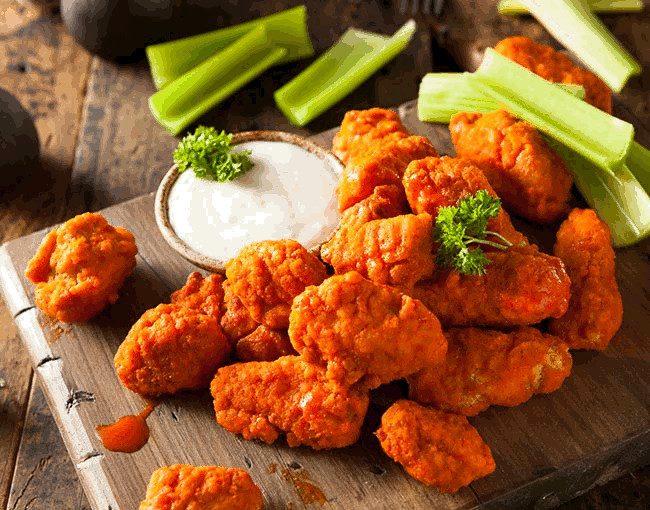 Buffalo-style boneless wings on a plate with celery and ranch sauce
