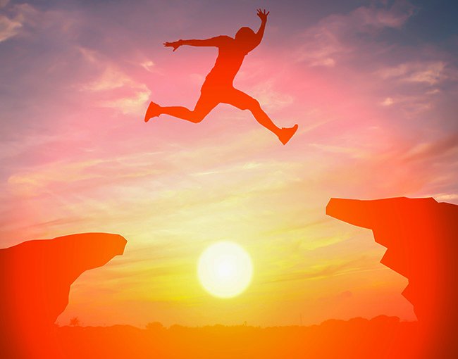 Man jumping from one cliff to another at sunset