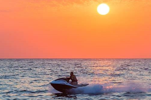 person driving a personal watercraft on open water with the sun setting