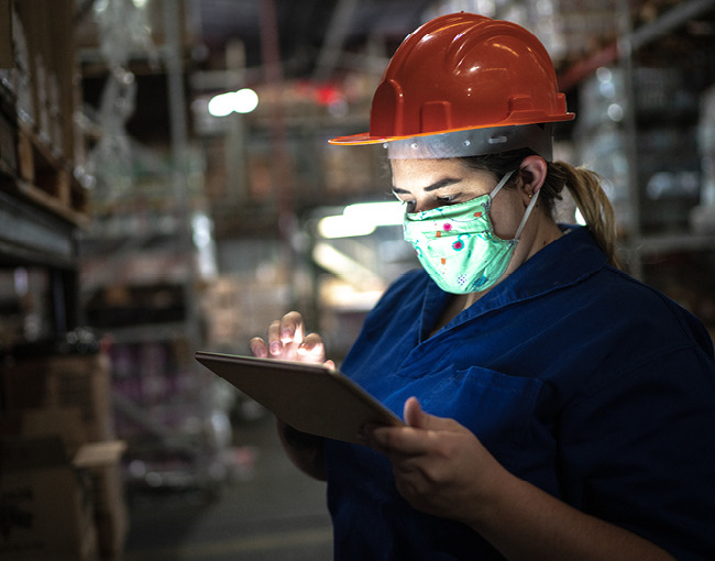 woman working in warehouse wearing hardhat and mask